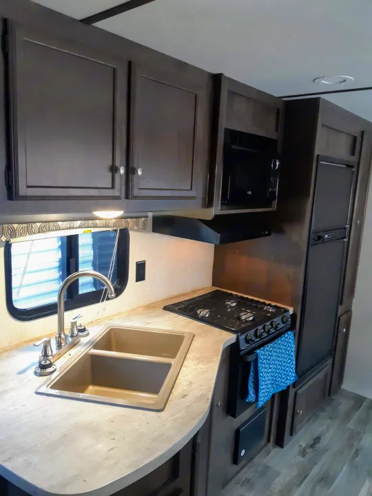 RV rental kitchen: Dark cabinets, light countertops, sink, stove, microwave, and refrigerator create a compact, functional space.. Starcraft Autumn Ridge 2018
