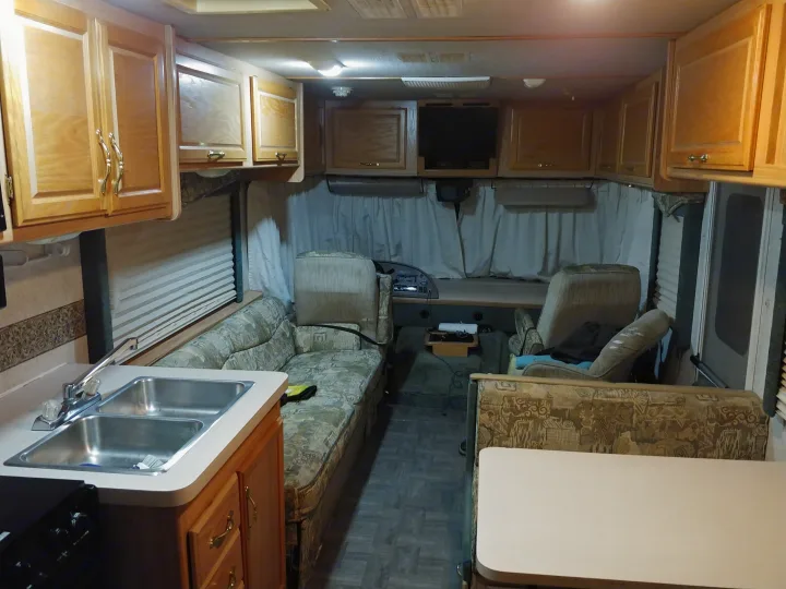 RV rental interior: kitchen with double sink, overhead cabinets, sofa, dining area, and front cockpit. Ready for adventures!. Fleetwood Flair 2000