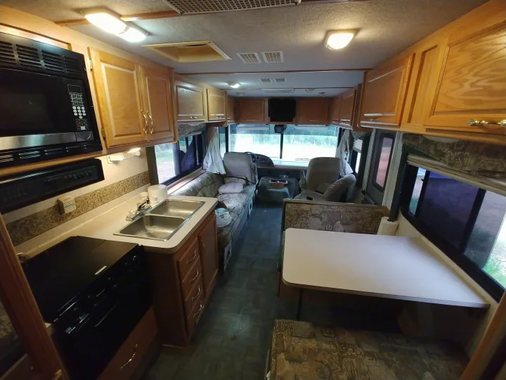 RV rental interior showing a kitchen with microwave, sink, and stove, plus dining area, overhead cabinets, and front seating.. Fleetwood Flair 2000