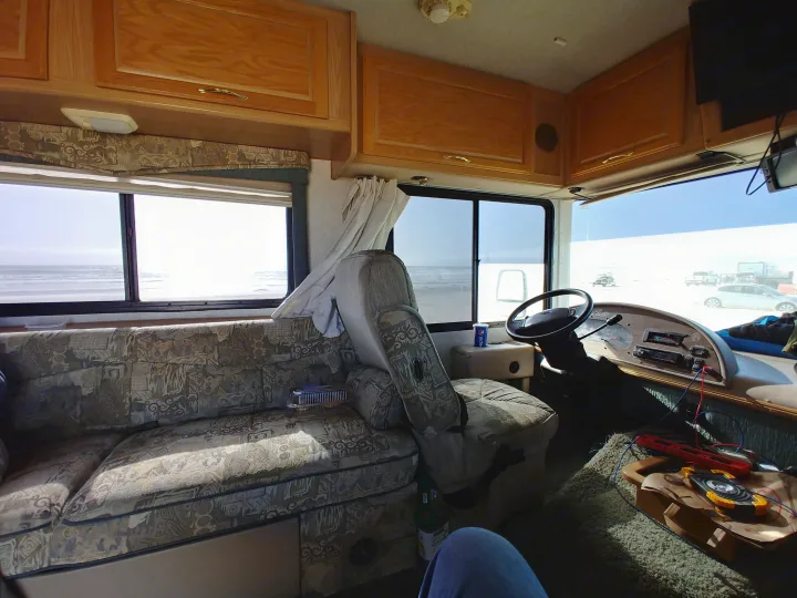 Interior of an RV rental showing a patterned sofa, dashboard, and bright windows with ocean and beach views.. Fleetwood Flair 2000