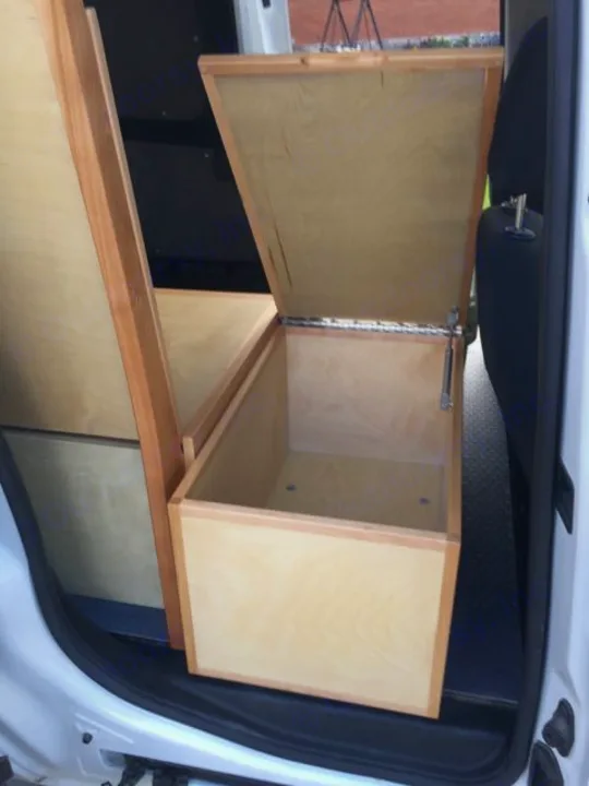 RV rental van interior features a custom wooden storage box with its lid open, showing practical built-in storage.. ram promaster city 2018