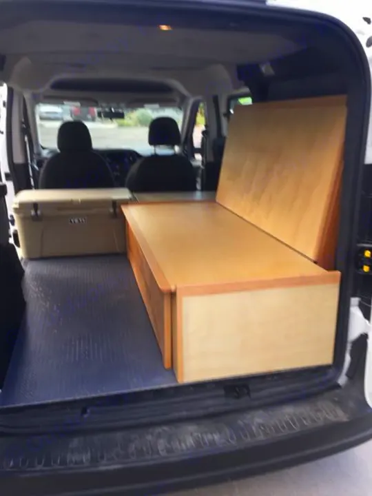 Inside an RV rental van: custom wooden bed, cooler, and front seats visible, ready for adventure.. ram promaster city 2018