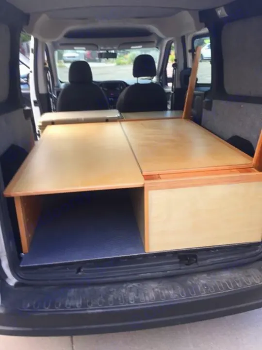 RV rental interior showcasing a wooden bed platform with under-storage. Perfect for compact campervan adventures.. ram promaster city 2018