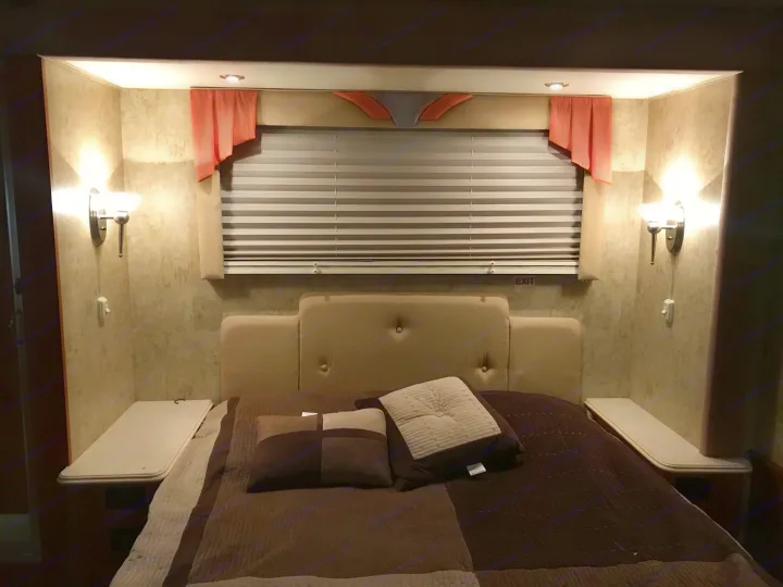 Inside an RV rental, this cozy bedroom features a comfortable bed, warm lighting, and window privacy for restful nights.. Dolphin 5342 2007