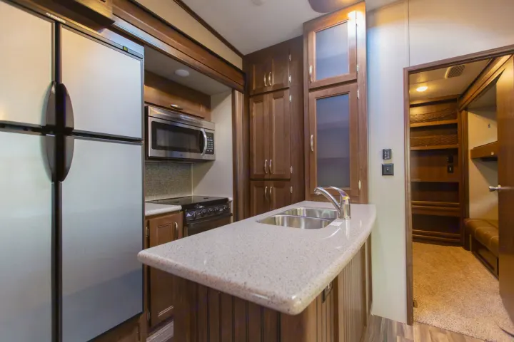 Well-equipped RV rental kitchen featuring fridge, microwave, sink island, and ample wood cabinetry.. Montana Mountaineer 2018