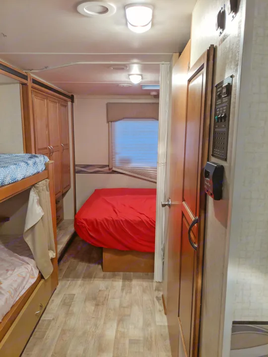 view from hall toward Master BR, passenger side pull out is extended. door to the bathroom and control panel visible on right side. bunk beds are on the left.  . Winnebago Minnie Winnie 2017
