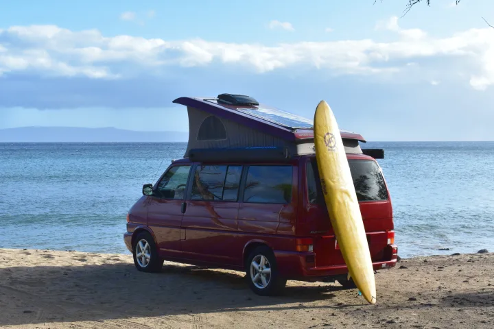 Red pop-top camper van RV rental with a surfboard, parked on a sandy beach by the ocean. Ready for island adventures!. Volkswagen Westfalia 2001