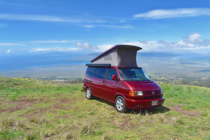 Red pop-top camper van rv rental on a grassy hill overlooking the blue ocean, islands, and coastline.. Volkswagen Westfalia 2001