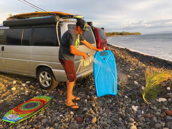 Enjoying the coast! A man uses an RV rental's outdoor shower to rinse his bodyboard after a day of beach fun.. Volkswagen Westfalia 2003