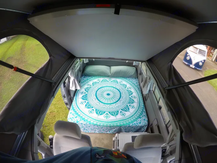 Cozy pop-top RV rental bed with mandala duvet, seen from inside the camper, overlooks a classic VW bus.. Volkswagen Westfalia 2003
