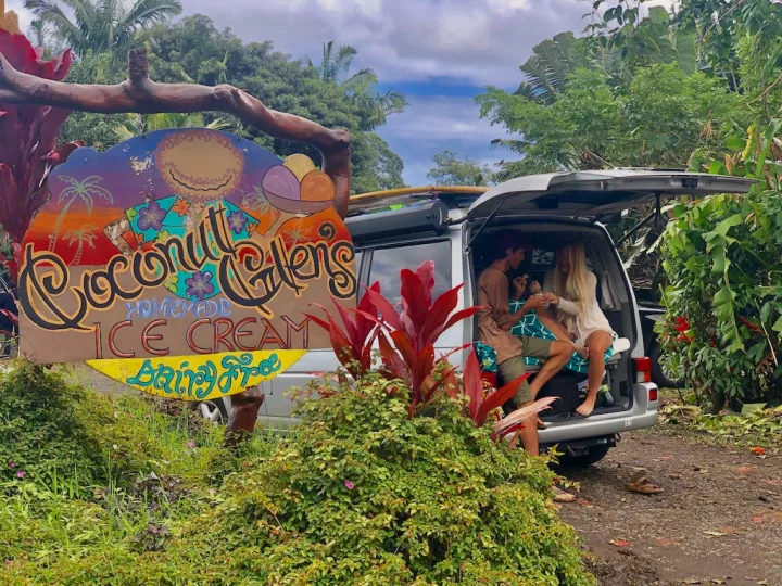Colorful Coconut Gardens Ice Cream sign beside an rv rental camper van with a couple relaxing inside, surrounded by lush tropics.. Volkswagen Westfalia 2002