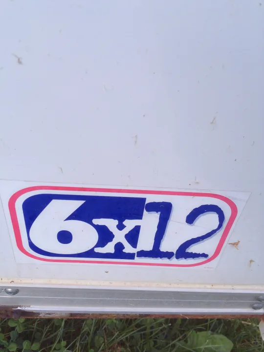 A blue and white "6X12" sticker with a red border is affixed to the white side of what appears to be an rv rental trailer.. Pace American Cargo Sport 2000