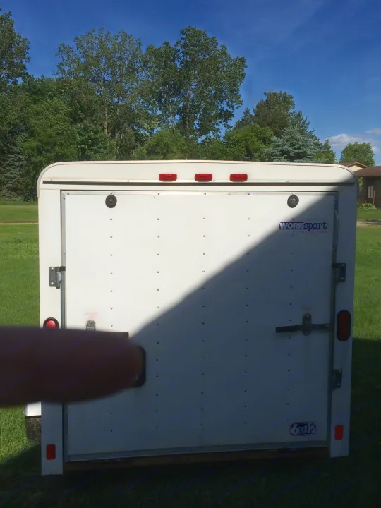 White enclosed cargo trailer with red lights, seen from the rear on a sunny day. Often used for gear with an rv rental.. Pace American Cargo Sport 2000