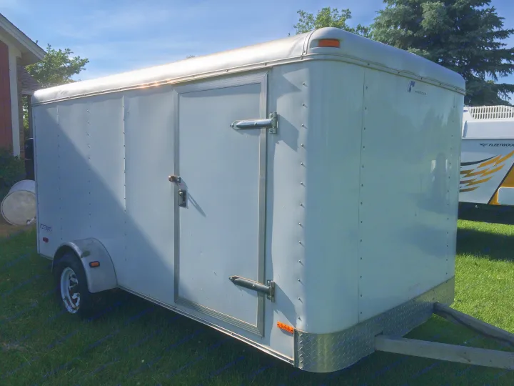 Light-colored enclosed utility trailer on green grass. Ideal for hauling cargo or as a great addition to your RV rental trip.. Pace American Cargo Sport 2000