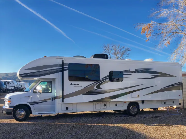 A white Jayco Greyhawk RV, perfect for rv rental adventures, is parked on a sunny gravel lot under a clear blue sky.. Jayco Greyhawk 2018