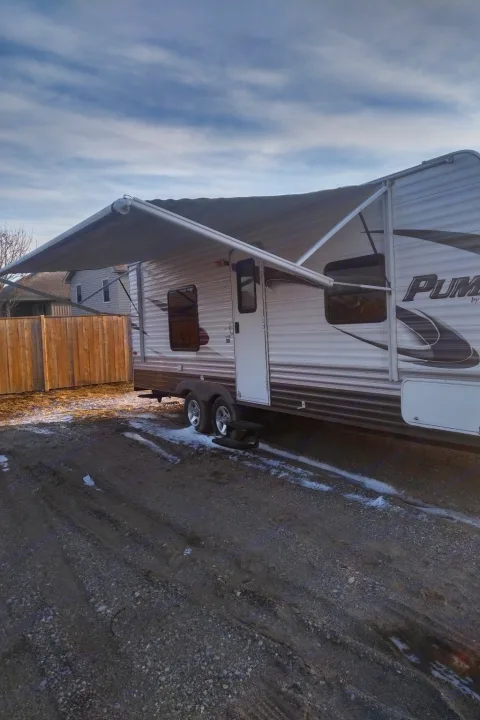 A white and brown travel trailer with its awning extended on gravel. Ideal RV rental for outdoor adventures.. Palamino Puma 23FB 2013