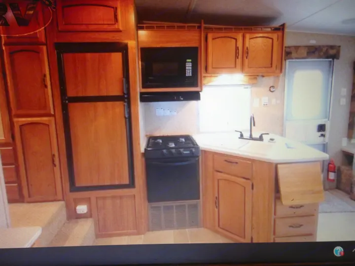 Compact RV rental kitchen showcasing a fridge, microwave, stove, sink, and wooden cabinetry.. Palomino Puma 2010