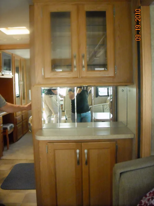 RV rental interior: A central wood cabinet unit with glass doors, counter, & mirrored section reflecting people and living space.. Thor Motor Coach Hurricane 34N 2006