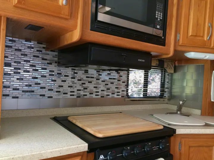 RV rental kitchen with oak cabinets, microwave, tiled backsplash, stove, cutting board, and sink.. Thor Motor Coach Hurricane 34N 2006