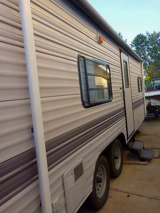 Exterior side of a grey RV travel trailer, featuring a window, door, and dual axles. Consider this for your next rv rental.. Skyline Nomad 1996