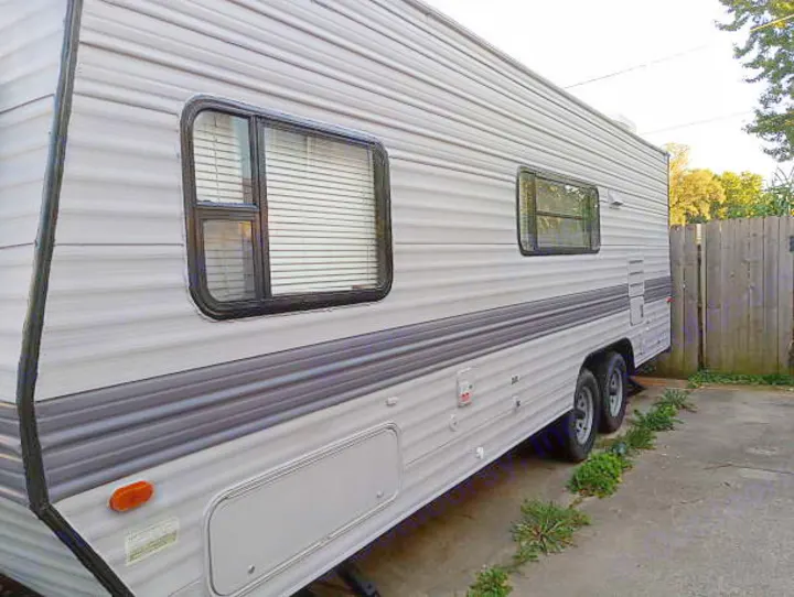 Gray travel trailer side view, ideal for an rv rental getaway. Features windows & parked near a fence.. Skyline Nomad 1996