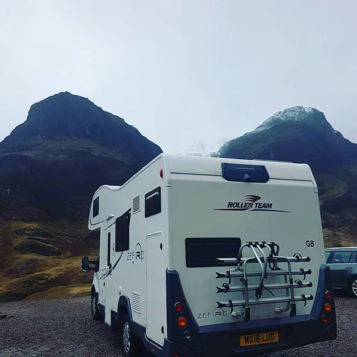 Ready for adventure! A white rv rental with a bike rack is parked on a gravel lot, surrounded by imposing, snow-dusted mountains.. Other Transit Motorhome 2018
