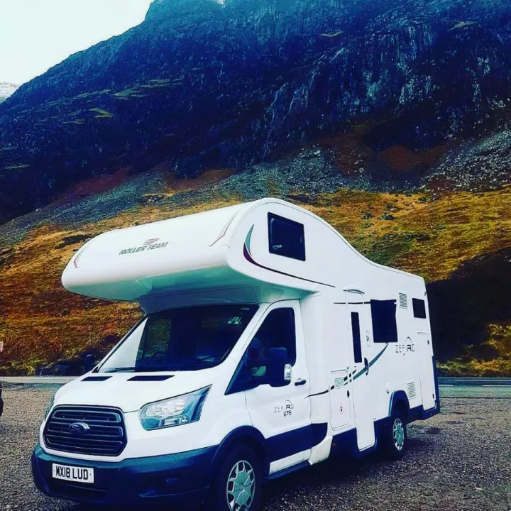 White RV rental campervan parked on a gravel lot with stunning dark mountains in the background, ready for scenic adventures.. Other Transit Motorhome 2018