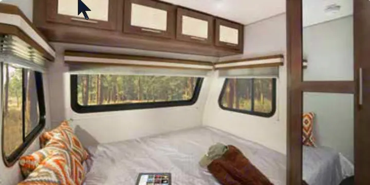 Cozy RV rental bedroom with a comfortable bed, overhead cabinets, and windows offering a forest view. Ideal for your next adventure.. Forest River Other 2019