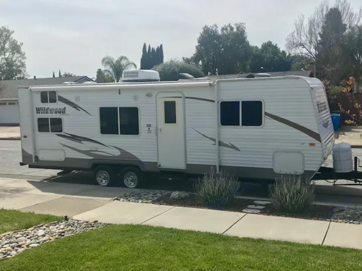 A large white Wildwood travel trailer, ideal for an rv rental, is parked curbside in a sunny residential neighborhood.. Wildwood Wildwood 2011