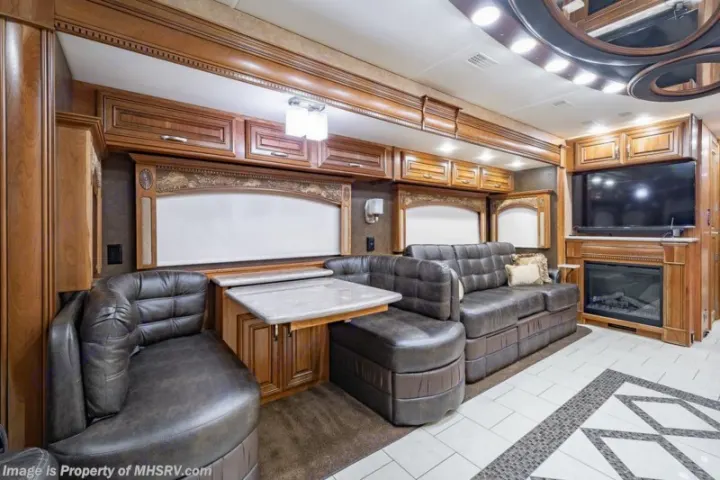 Plush leather seating and dining nook inside a high-end RV rental. Features TV, fireplace, and ornate woodwork.. Entegra Coach Anthem 44dlq 2016
