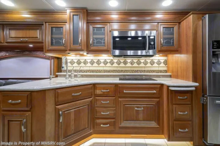 Modern RV rental kitchen features rich wood cabinets, stainless steel microwave, sink, and stovetop. Well-lit interior.. Entegra Coach Anthem 44dlq 2016