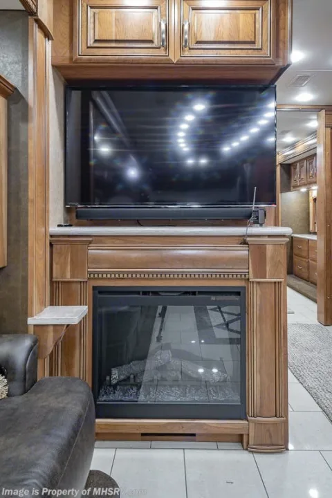 Luxury RV rental interior with entertainment center: TV, soundbar, and electric fireplace in rich wood cabinetry.. Entegra Coach Anthem 44dlq 2016