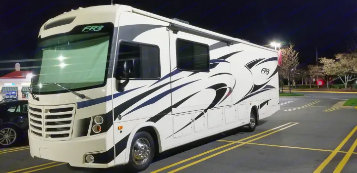 Large white Class A Forest River FR3 RV, ideal for an rv rental, parked at night in a lighted lot.. Forest River Fr3 2021