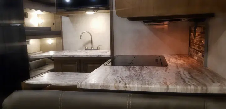 RV rental interior: A well-lit kitchen with patterned counters, sink, stovetop, dining booth, and bunk beds visible.. Forest River Fr3 2021