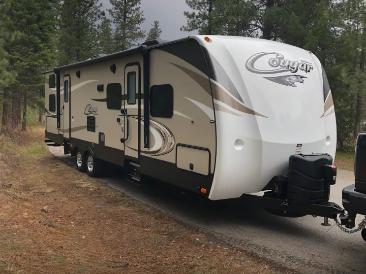 A Cougar travel trailer, ideal as an RV rental, parked for camping in a scenic, wooded setting.. Keystone Cougar 2018