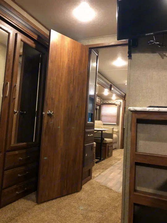 RV rental interior: Wooden wardrobe, open door, and dinette visible in the compact living space. Well-lit.. Keystone Cougar 2018