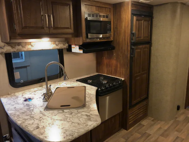 RV rental kitchen interior: modern sink, stovetop, microwave, and refrigerator, with stylish counters and wood cabinetry.. Keystone Cougar 2018
