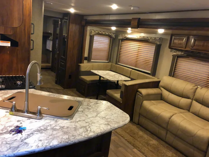 This bright RV rental interior features a modern kitchen, comfortable dinette & sofa, plus a bunk area visible through a doorway. Keys are on the counter.. Keystone Cougar 2018