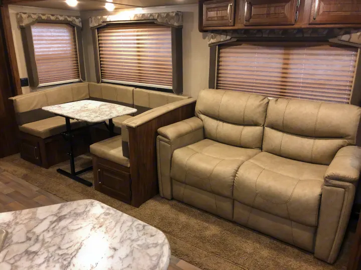 Cozy RV rental interior: U-shaped dinette, light sofa, windows with blinds, and overhead cabinets for a comfortable stay.. Keystone Cougar 2018