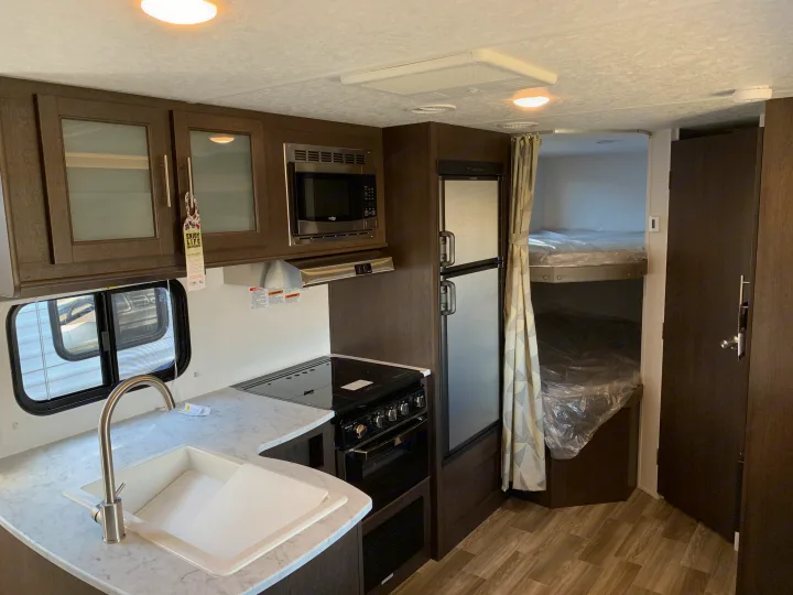 Compact RV rental interior featuring a well-equipped kitchen with sink, stove, microwave, refrigerator, and convenient bunk beds.. Forest River Cruise Lite 2020