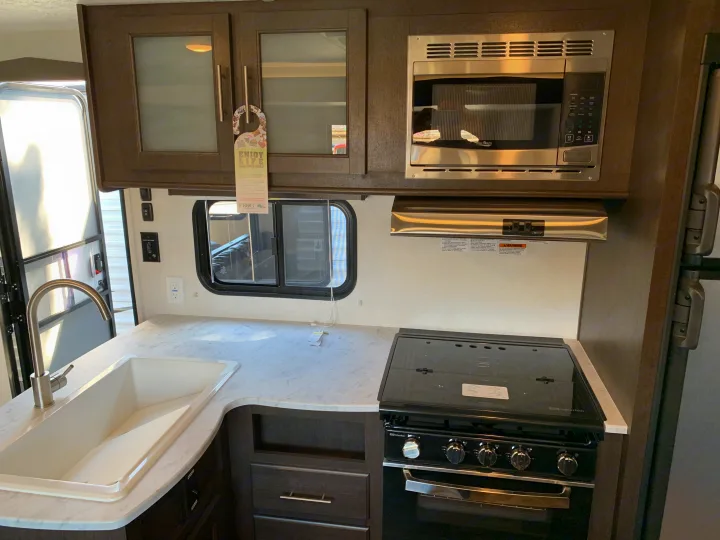 This RV rental kitchen offers a practical layout with a sink, microwave, and Suburban stove, ideal for enjoying life on the open road.. Forest River Cruise Lite 2020