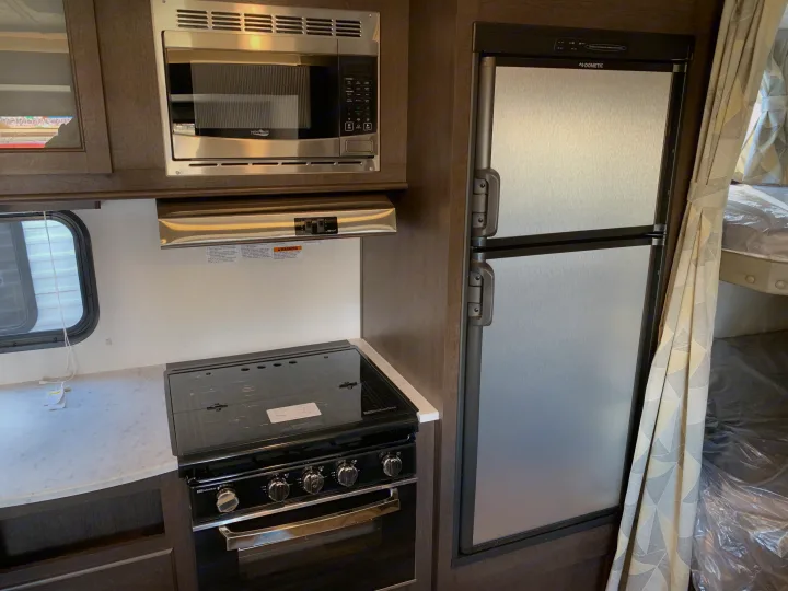 Compact RV rental kitchen with stainless appliances: High Pointe microwave, Suburban stove, and Dometic refrigerator.. Forest River Cruise Lite 2020