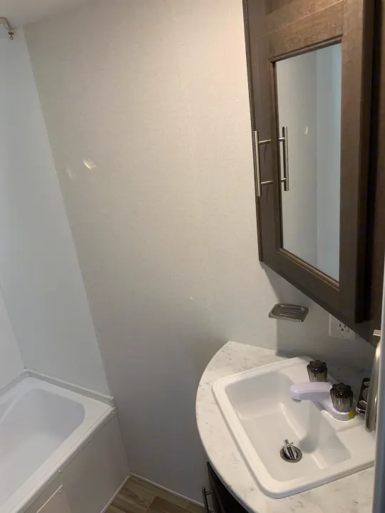 An RV rental's compact bathroom features a white sink, mirror, and small bathtub, designed for efficient use of space.. Forest River Cruise Lite 2020