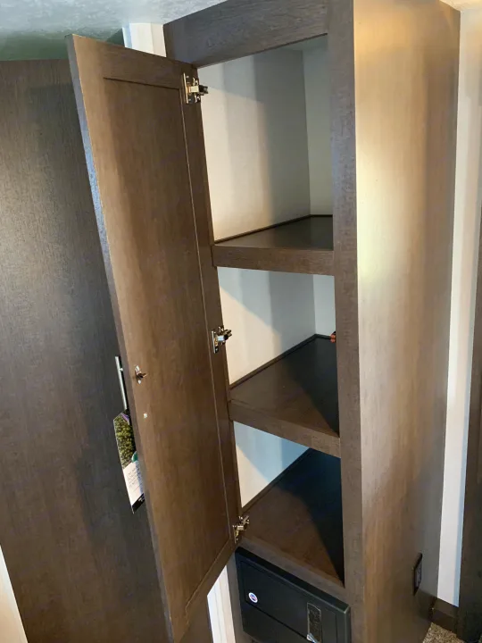 RV rental: Open dark wood cabinet with empty shelves and a bottom control panel, offering storage space.. Forest River Cruise Lite 2020