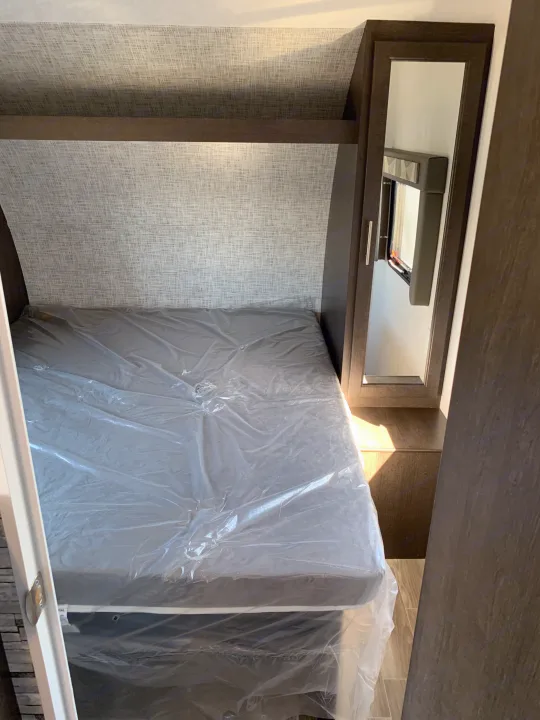 Compact RV rental bedroom featuring a mattress in plastic, textured walls, and a built-in cabinet with mirror.. Forest River Cruise Lite 2020