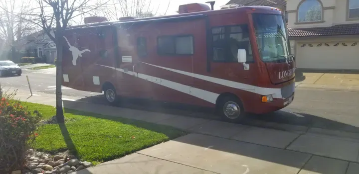 A prominent reddish-brown RV with white Texas Longhorns logo and 'LONGHORN' text, parked on a residential street for rv rental.. Winnebago Vista 2013