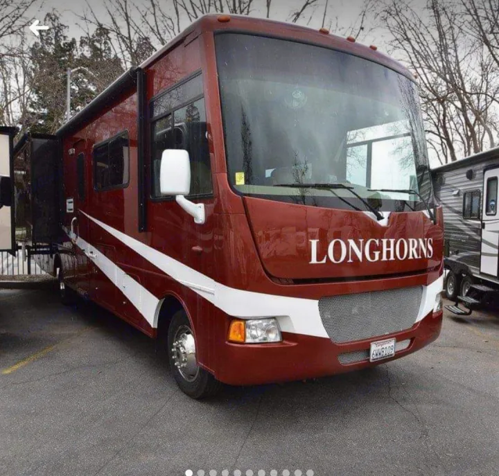 This red "LONGHORNS" RV rental, a Class A motorhome with white side stripes, is parked and ready for travel.. Winnebago Vista 2013