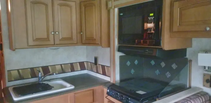 An RV rental kitchen featuring light wood cabinets, a sink, microwave, and stove. Essential for mobile living.. Winnebago Vista 2013