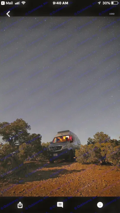 A dark night scene with a camper van (RV rental) under a starry sky. Inside, warm lights glow, parked amidst trees on a dirt road.. Winnebago Mercedes Sprinter 2019