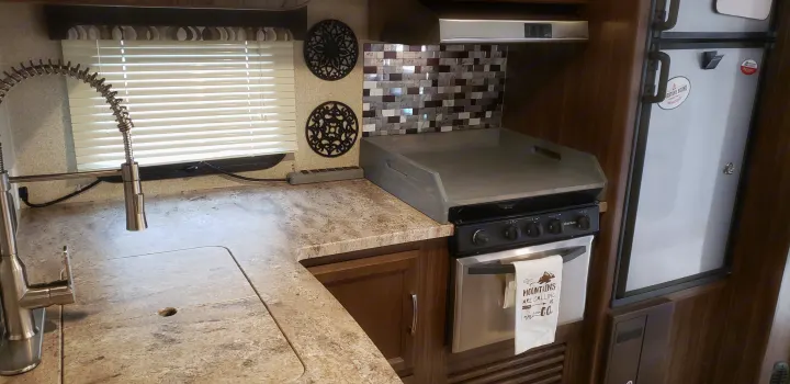 Inside an RV rental, a well-equipped kitchen features a sink, stove/oven, refrigerator, and custom stovetop cover.. Coachmen Apex 265rbss 2019